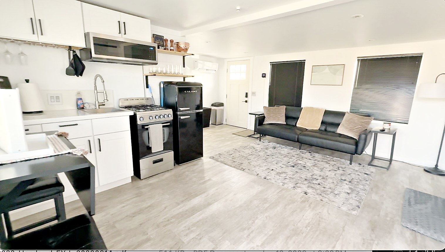 Open living room with black leather sofa and kitchen beyond